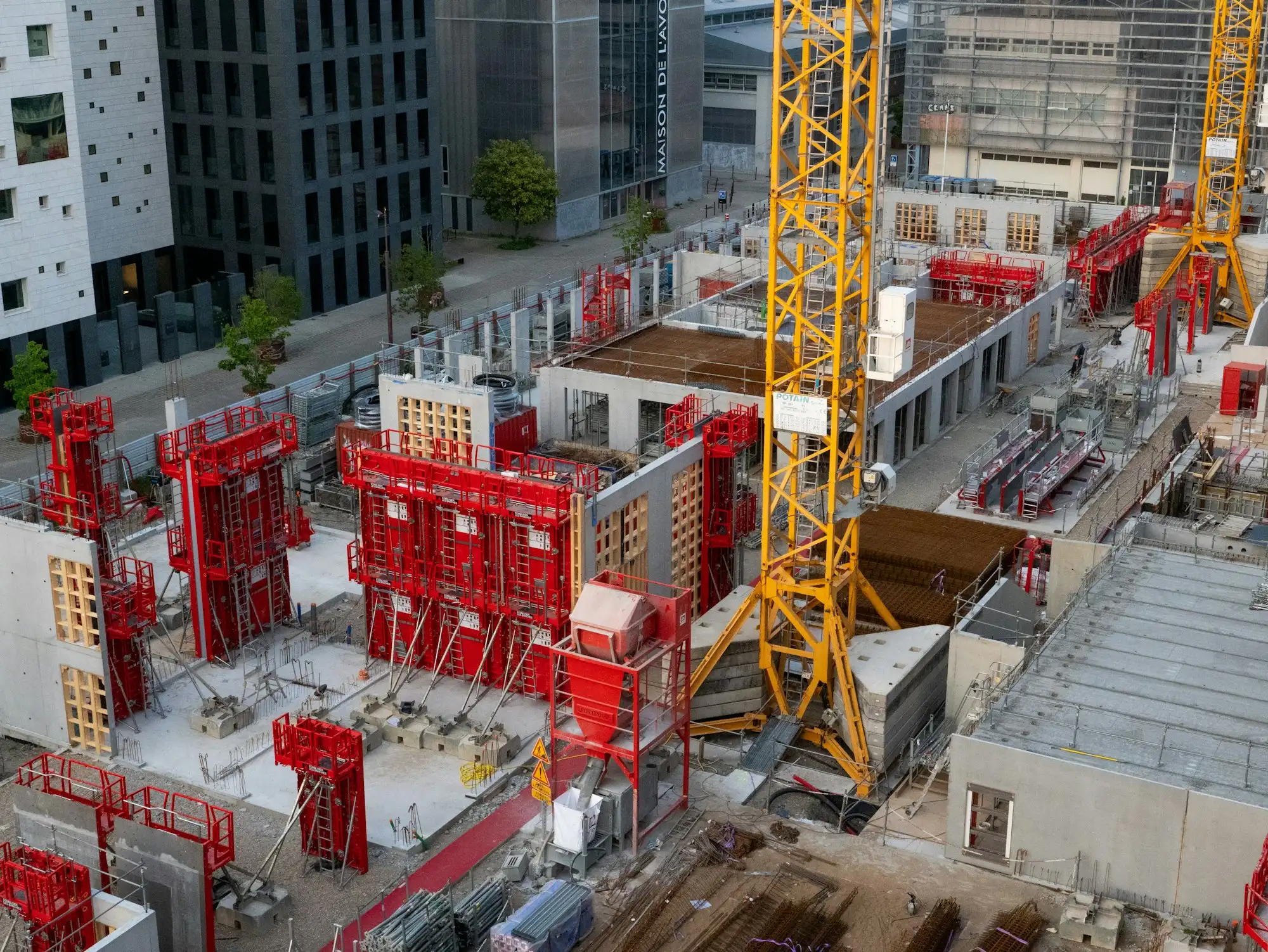 Chantier de gros œuvre vu d’en haut, avec grue à tour, banches de coffrage et voiles en béton.