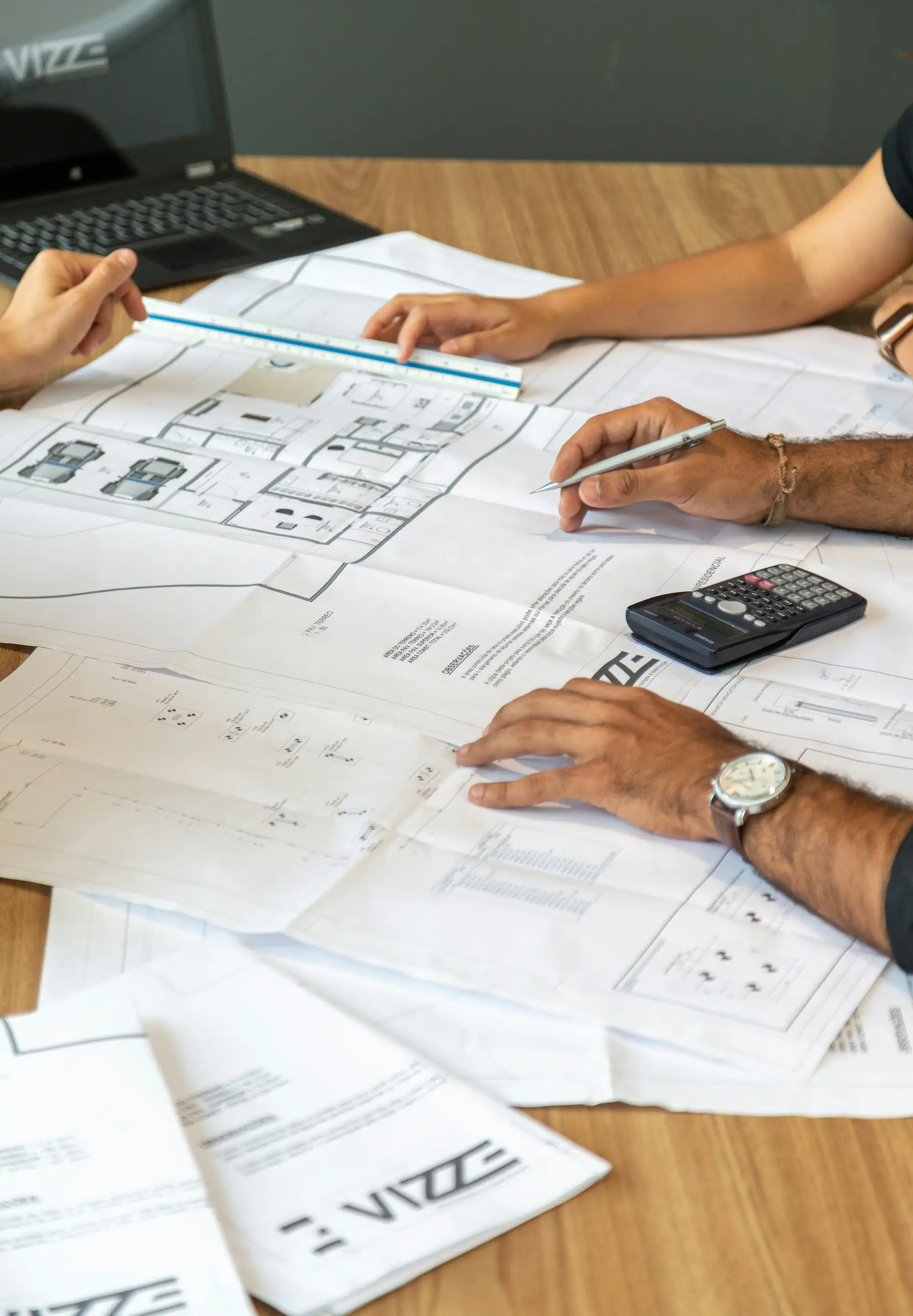 Plans de construction étalés sur une table, avec règle d’architecte et calculatrice.